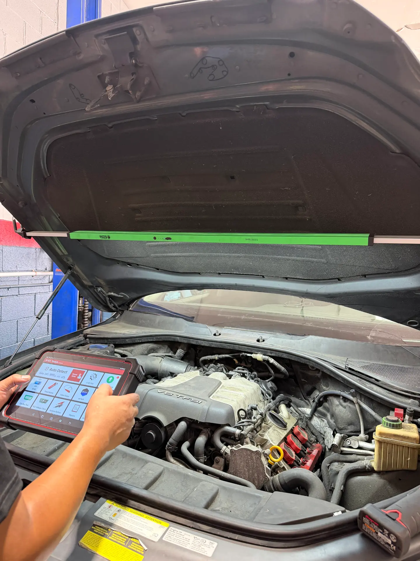 Close-up of a technician using a diagnostic tablet beside a V6 engine during an automotive electronics check