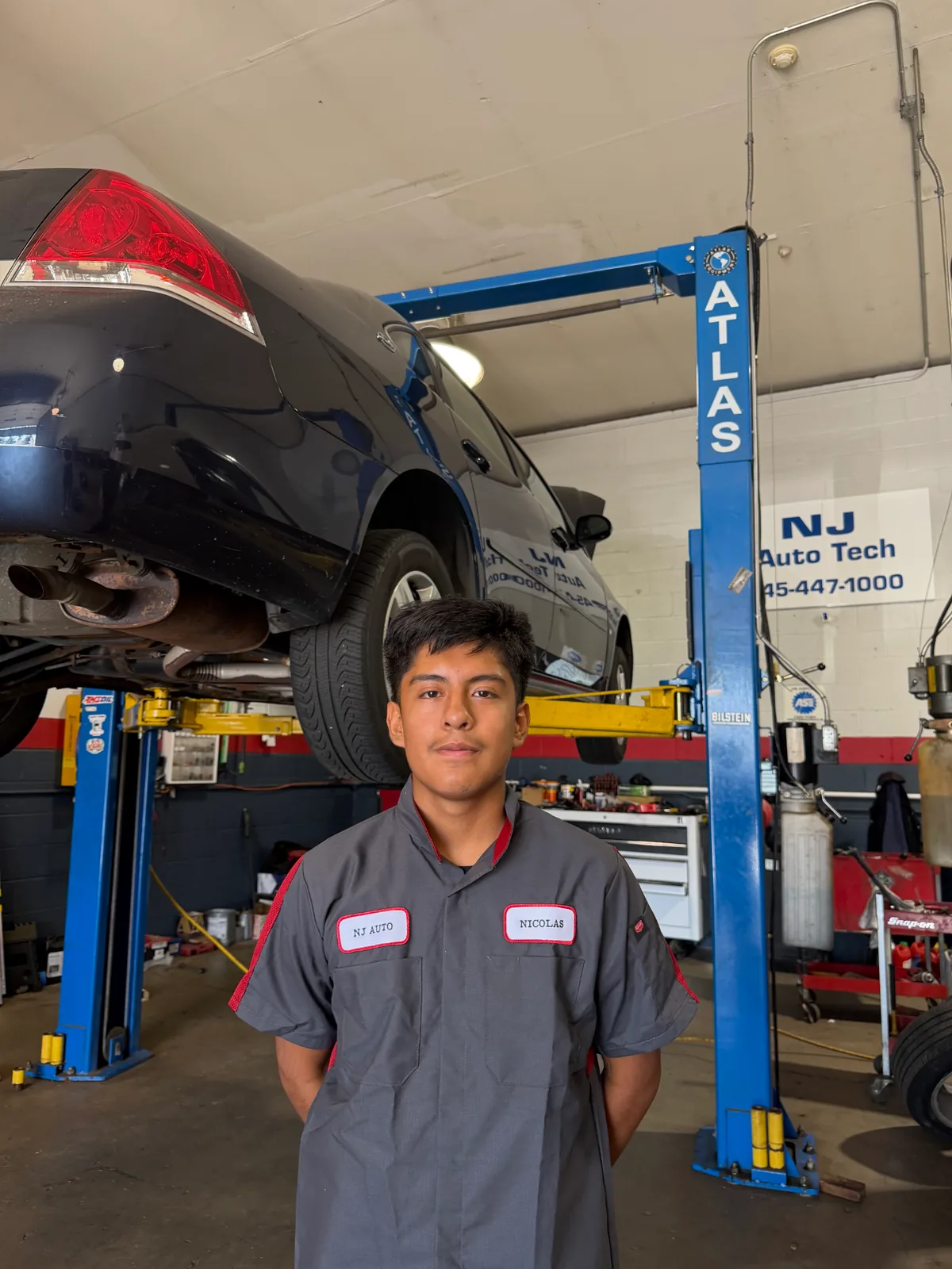Technician Nicolas standing beside a sedan raised on the Atlas lift inside the shop