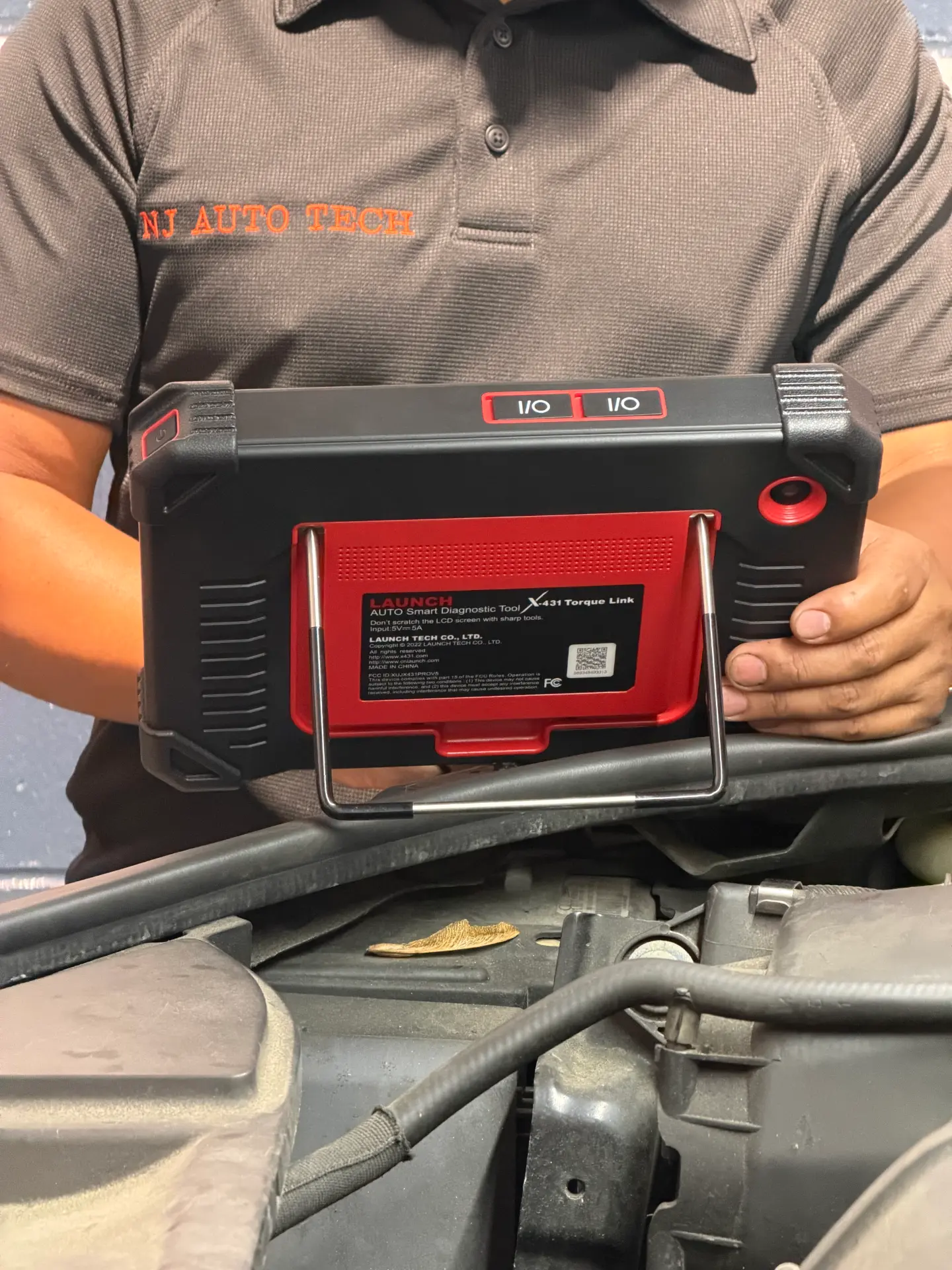 NJ Auto Tech technician holding a Launch X-431 smart diagnostic scan tool over an open engine bay