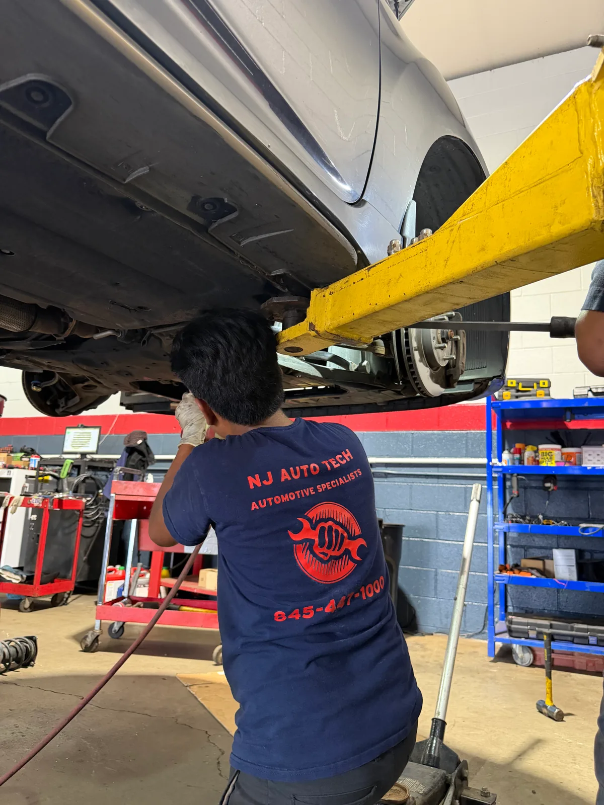 Technician working under a raised vehicle on suspension and brake components in Wappingers Falls, NY